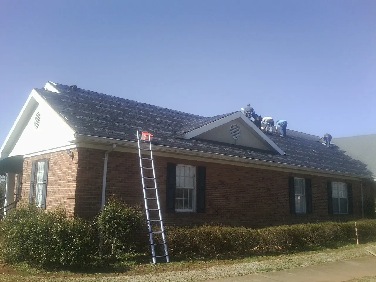 Crew tearing shingles off a brick ranch roof with a ladder set — Metal Roof Repair work by our crew in Eagle Mountain