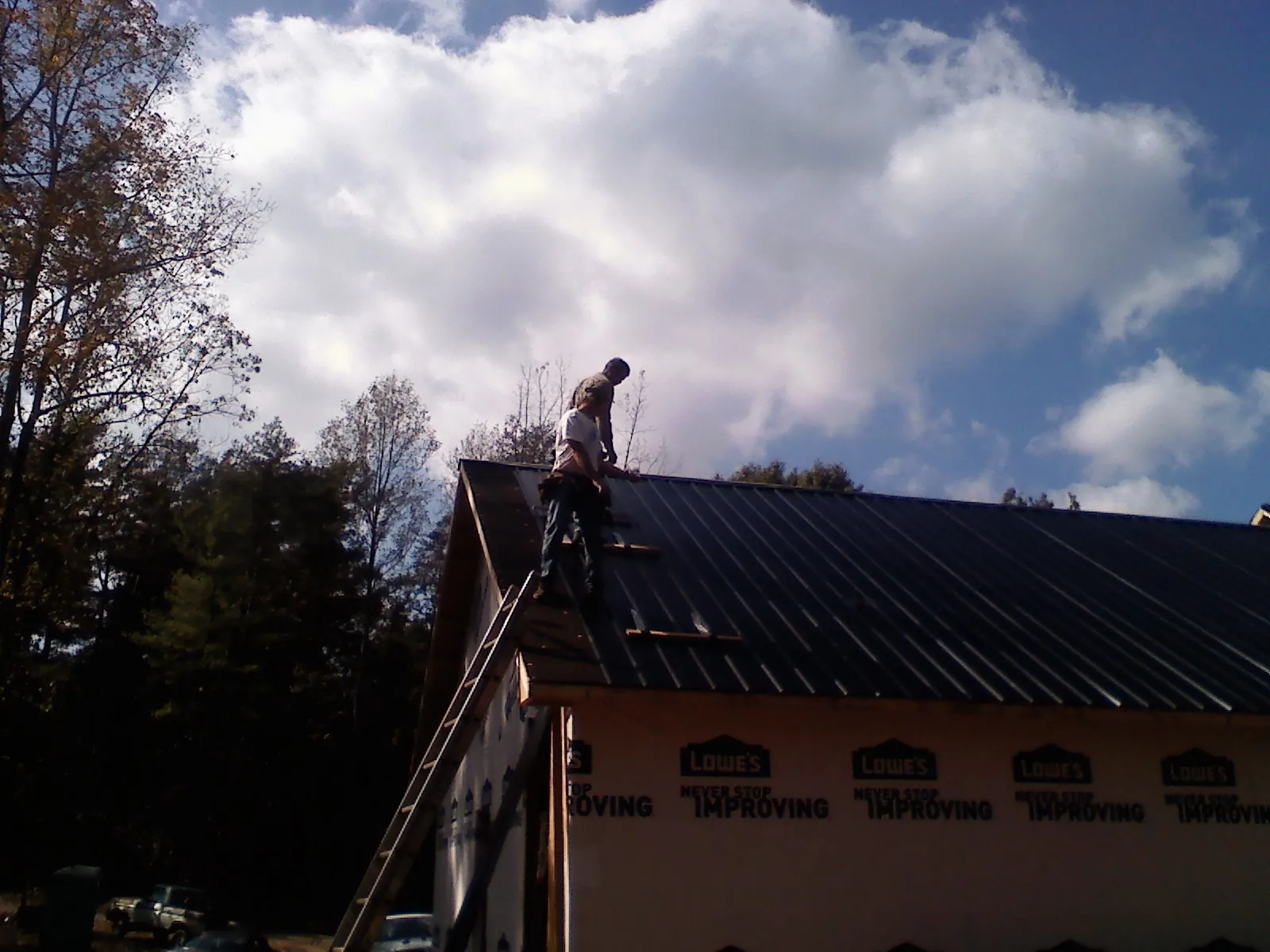 Roofer fastening dark metal panels high against a cloudy sky, from a Roof Inspection job in Eagle Mountain