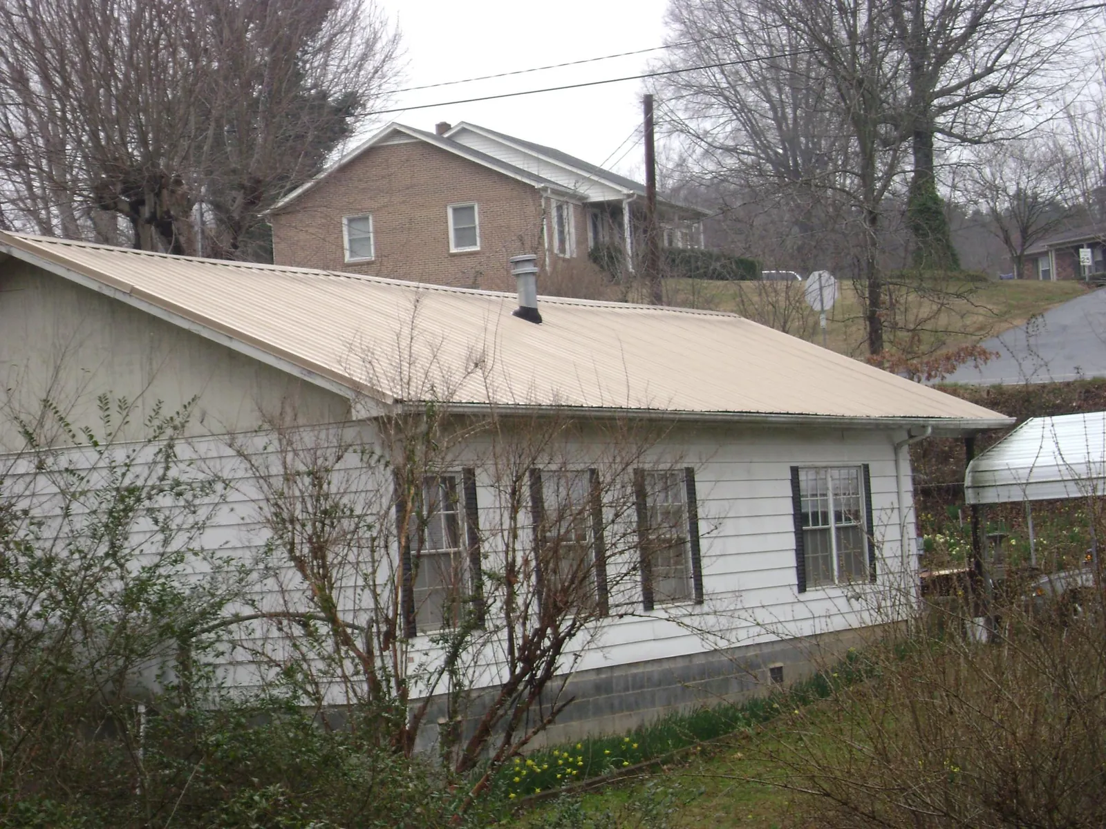 Tan metal roof on a white sided house set into a hillside — Commercial Roofing by Roofing Brothers in Eagle Mountain